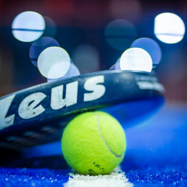 Nahaufnahme eines Tennisschl&auml;gers mit gelbem Tennisball auf einer blauen Spielfeldmarkierung.