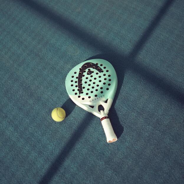 Tischtennisschl&auml;ger mit L&ouml;chern und gelbem Ball auf einer blauen Tischtennisplatte.