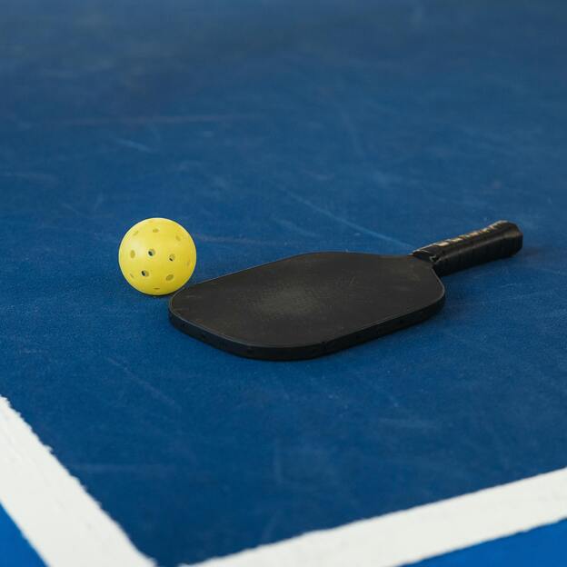 Schwarzer Tischtennisschl&auml;ger und gelber Ball auf einer blauen Tischtennisplatte mit wei&szlig;en Linien.