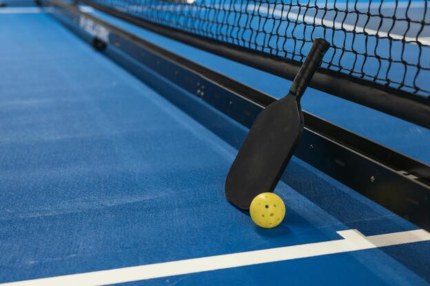 Nahaufnahme eines Paddles und eines gelben Balls neben einem Netz auf einem blauen Spielfeld.