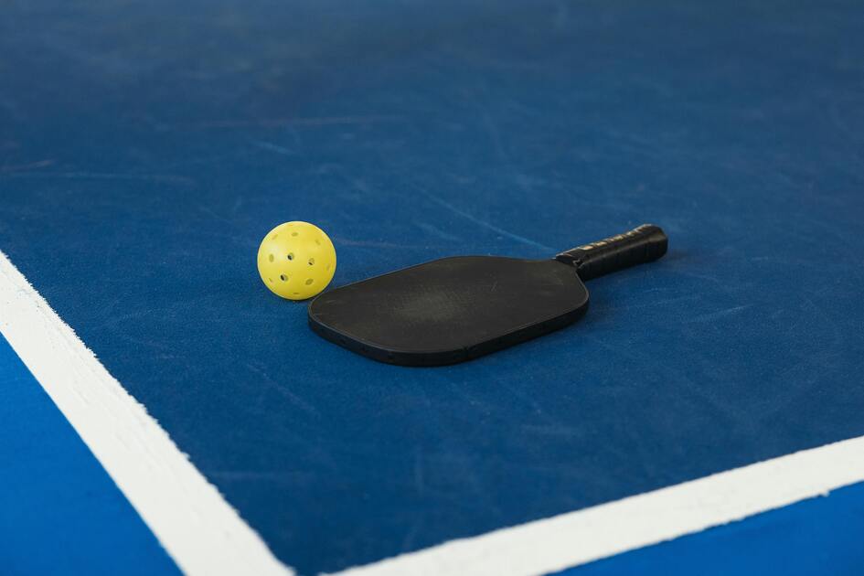 Schwarzer Tischtennisschl&auml;ger und gelber Ball liegen auf einer blauen Tischtennisplatte.